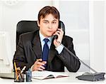 Thoughtful modern business man talking on phone and making notes in diary