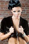 fashion portrait of a cute brunette wearing a brown fur and jewellery near a brick wall