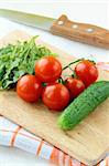 ingredients for the salad cucumber tomato and arugula on the kitchen board