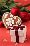 Little gift box with gingerbread heart and red roses in background