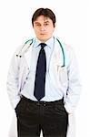 Serious doctor with stethoscope keeping his hands in pockets isolated on white