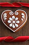 Gingerbread heart and red ribbon on brown wooden background. Shallow dof