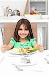 Adorable llittle girl holding forks to eat pasta and salad in the kitchen