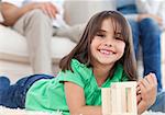 Cute little girl playing with dominoes in the living room with her parents