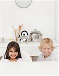 Happy brother and sister waiting their breakfast sitting in the kitchen