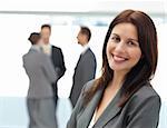 Pretty businesswoman posing in front of her team while working in the background