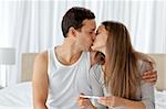 Couple kissing after looking at the result of a pregnancy test in the bedroom