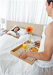 Lovely man bringing the breakfast to his girlfriend lying on the bed at home