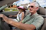 A happy senior couple driving a convertible car wearing sunglasses
