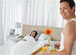 Happy man bringing the breakfast to his girlfriend on the bed at home