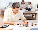 Man calculating his bills while his family are on the sofa