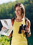 young caucasian female hiker reading map and holding binoculars. Vertical shape, waist up, front view
