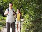 senior man and young woman walking with backpack in wood, looking at camera and smiling. Horizontal shape, front view, copy space
