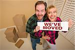 Goofy Couple Holding We've Moved Sign in Room with Packed Cardboard Boxes.