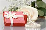 Gift box with pearl necklace near cream rose with reflection