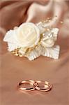 Wedding rings on silk background aganst satin rose