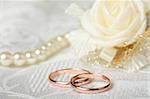 Wedding rings on lace background with goldev satin rose and pearl necklace