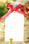 Blank gift tag tied with a bow of red satin ribbon against christmas background