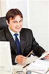 Smiling business man sitting at office desk and working with documents