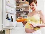 italian 6 months pregnant woman standing near refrigerator and drinking orange juice. Waist up, horizontal shape
