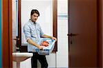 portrait of adult caucasian man leaning on washing machine and looking at camera with clothes basket. Horizontal shape, side view, copy space