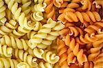 Two flavors of fusilli pasta. Italian food background.