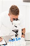 Laboraratory woirk: young researcher looks in microscope and takes notes