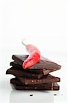 Red chili pepper on stack of dark chocolate pieces on white background. Shallow dof