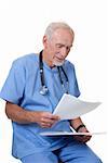 A senior medical practitioner in blue scrubs is sitting on a stool, looking over his patient's notes.