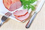 Smoked ham and dill on white plate with knife and fork on a bamboo mat