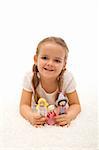 Happy little girl playing with her puppets family laying on the floor - isolated