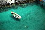 A lone row boat floating in clear, blue water.