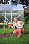 young pretty gardening woman with rakes outdoors near greenhouse