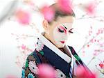 Artistic portrait of japan geisha woman with creative make-up near sakura tree