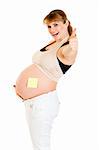 Smiling pregnant woman with blank sticky note on her belly showing thumbs up gesture isolated on white