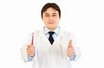 Smiling dentist holding toothbrush and showing  thumbs up gesture  isolated on white