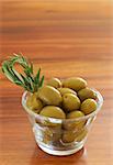 Jar of green olives and rosemary on wooden table background