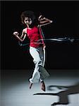 young adult latin american female jumping and playing with led lights doing streaks on black background. Vertical shape, full length, front view, copy space