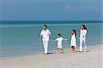 A happy family of mother, father and two children, son and daughter, walking and holding hands on a sunny tropical beach