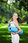 Young girl with a gym mat and a bottle of water in the park