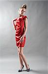 Young fashionable model in red dress at grey background