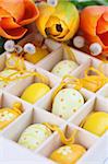 Yellow Easter eggs in a box and colorful tulips. Shallow dof