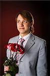 Young man wearing suit holding roses over red background