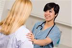Smiling Attractive Multi-ethnic Young Female Doctor or Nurse Wearing Scrubs and Stethoscope Talking with Patient.