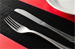empty white plate on red napkin with knife and fork on black table at the side of the plate