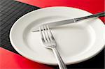 empty white plate on black table with knife and fork on the plate and red napkins by the sides of the plate