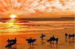 surfers walking on the beach in lahinch county clare ireland as the sun goes down