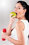 sporty woman is biting off green apple on grey background