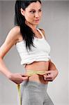 sporty woman is measuring her waist on grey background