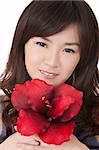 Asian girl holding red flower and looking at you, closeup portrait.